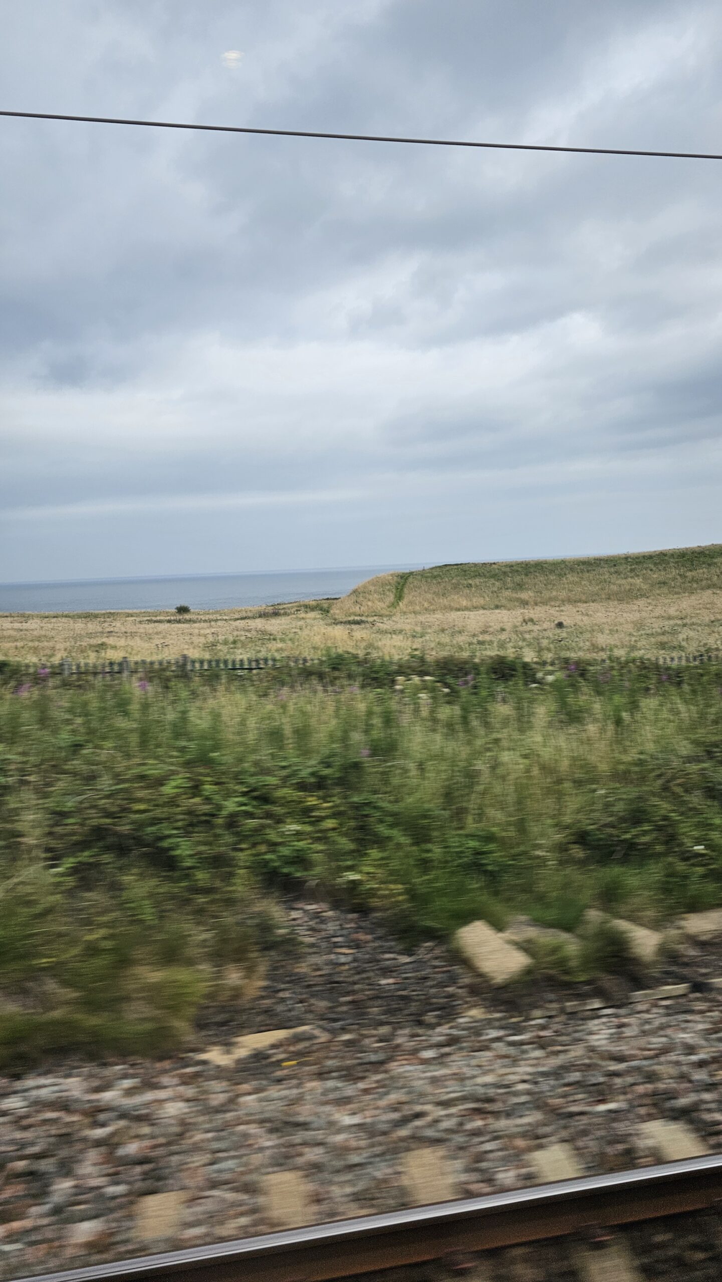 Paisagem costeira com mar ao fundo vista pela janela do trem no trajeto Londres a Edimburgo