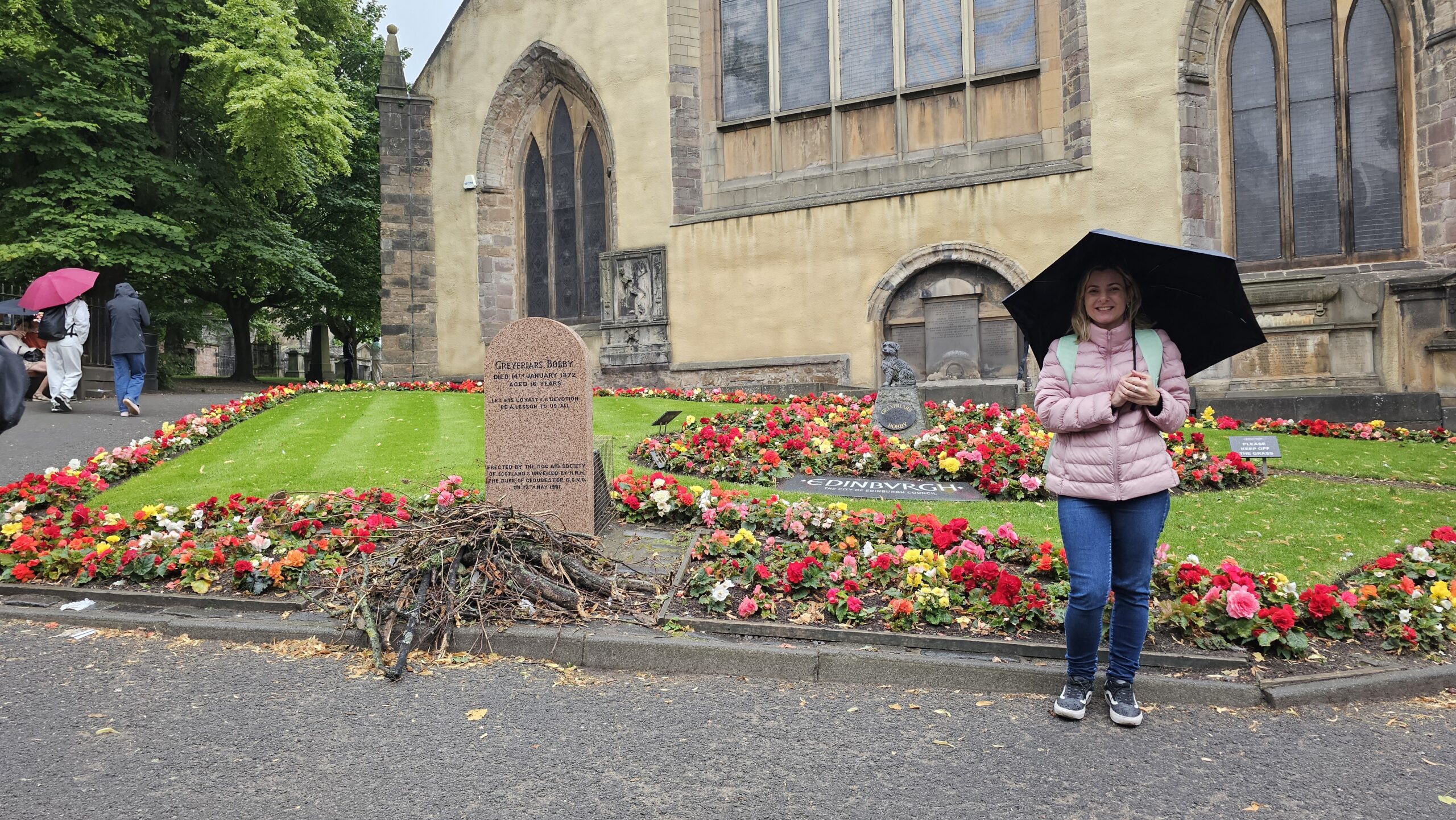 Lápide de granito vermelho do Greyfriars Bobby com gravetos e presentes deixados por visitantes.